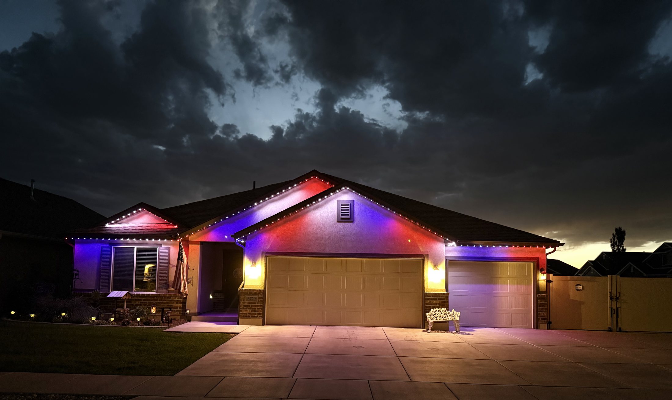 A single-story rambler at night with Aurora lights washing its roofline in red, white and blue