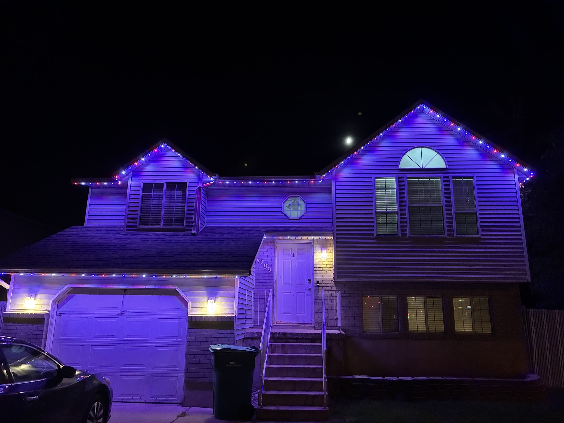 Two-story home with red, white and blue bulbs casting a violet wash over the siding