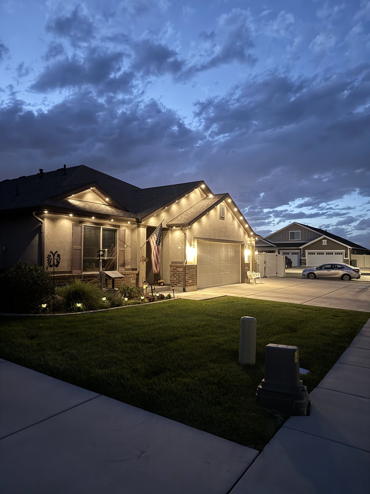Side view of a single-story rambler at dusk with warm white Aurora lights along the eaves and gables